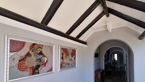A hallway with two mosaic artworks on the wall, a wooden bench, and an arched doorway leading to another room. - Villa Venusta (Hermanus)