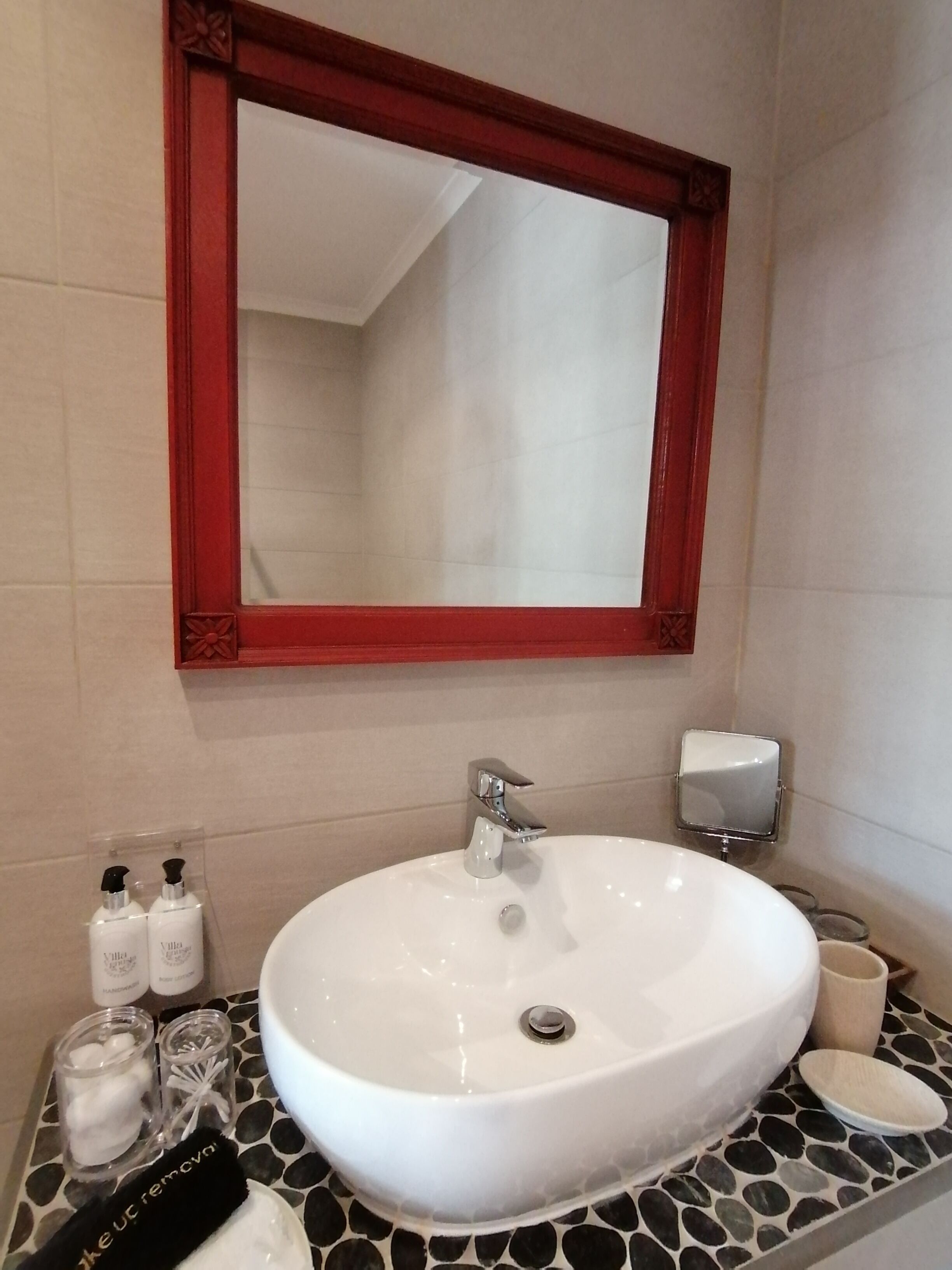A bathroom with a white sink, a red-framed mirror, and toiletries on the counter.