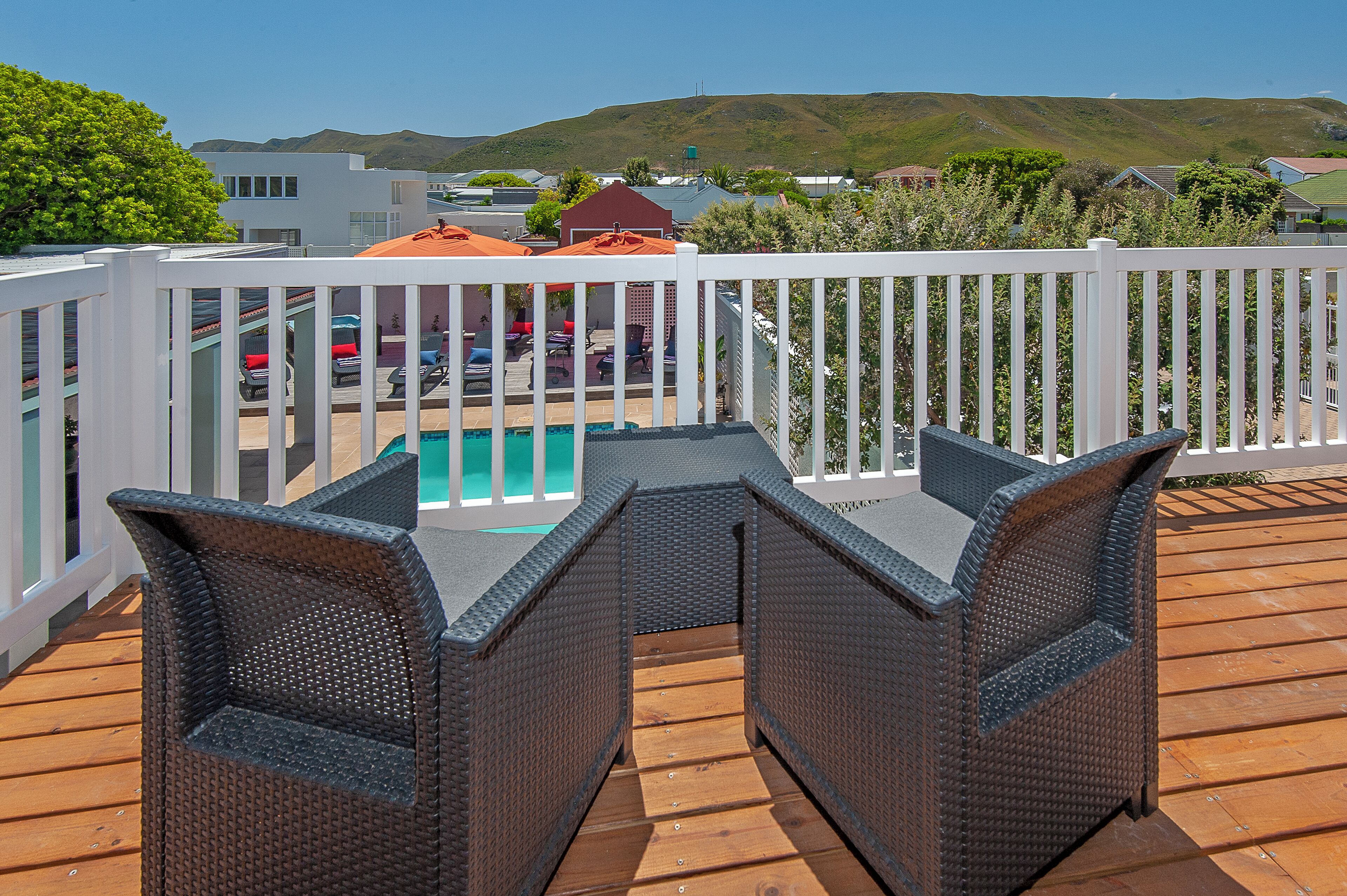 Une terrasse dotée de meubles en osier et d’une piscine, le tout entouré d’une clôture blanche.