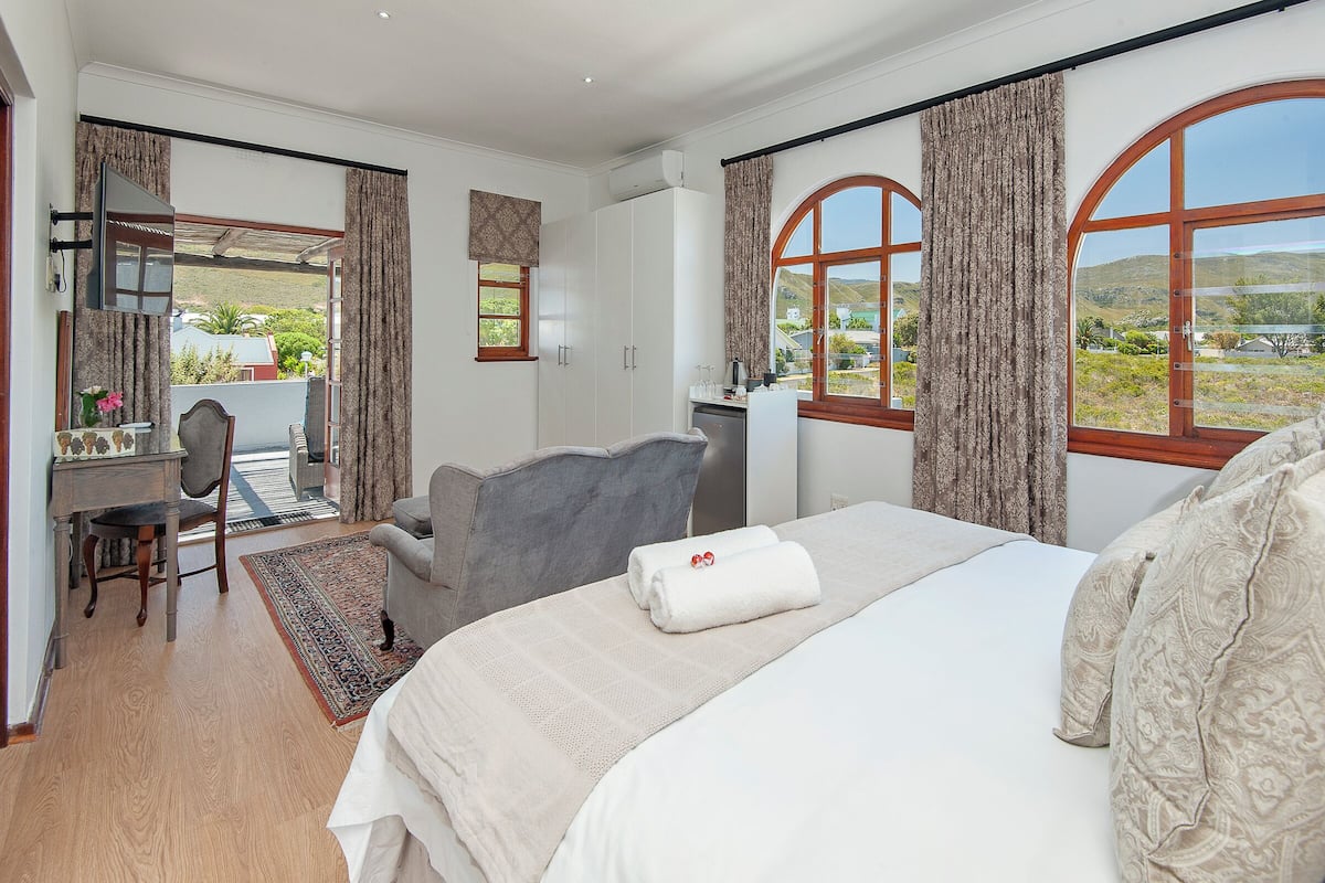 A hotel room with a bed, a desk, a chair, and large windows offering a view of the outdoors.