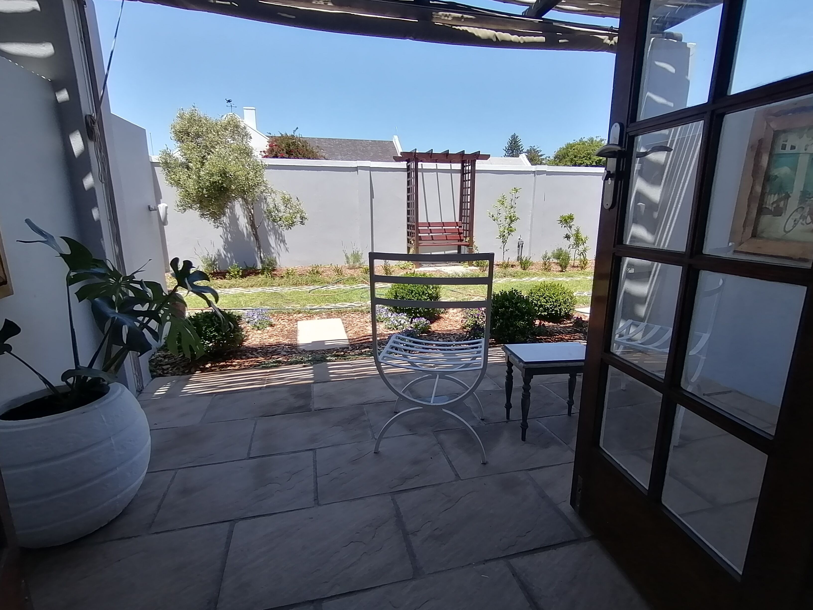 Eine Terrasse mit Steinplatten, einem Metallstuhl, einem Holzstuhl und Topfpflanzen.