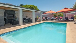 A swimming pool with lounge chairs and umbrellas, a barbecue area, and a covered patio. - Villa Venusta (Hermanus)