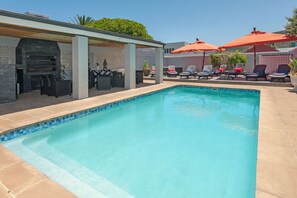 Una piscina al aire libre, sombrillas, sillones reclinables de piscina