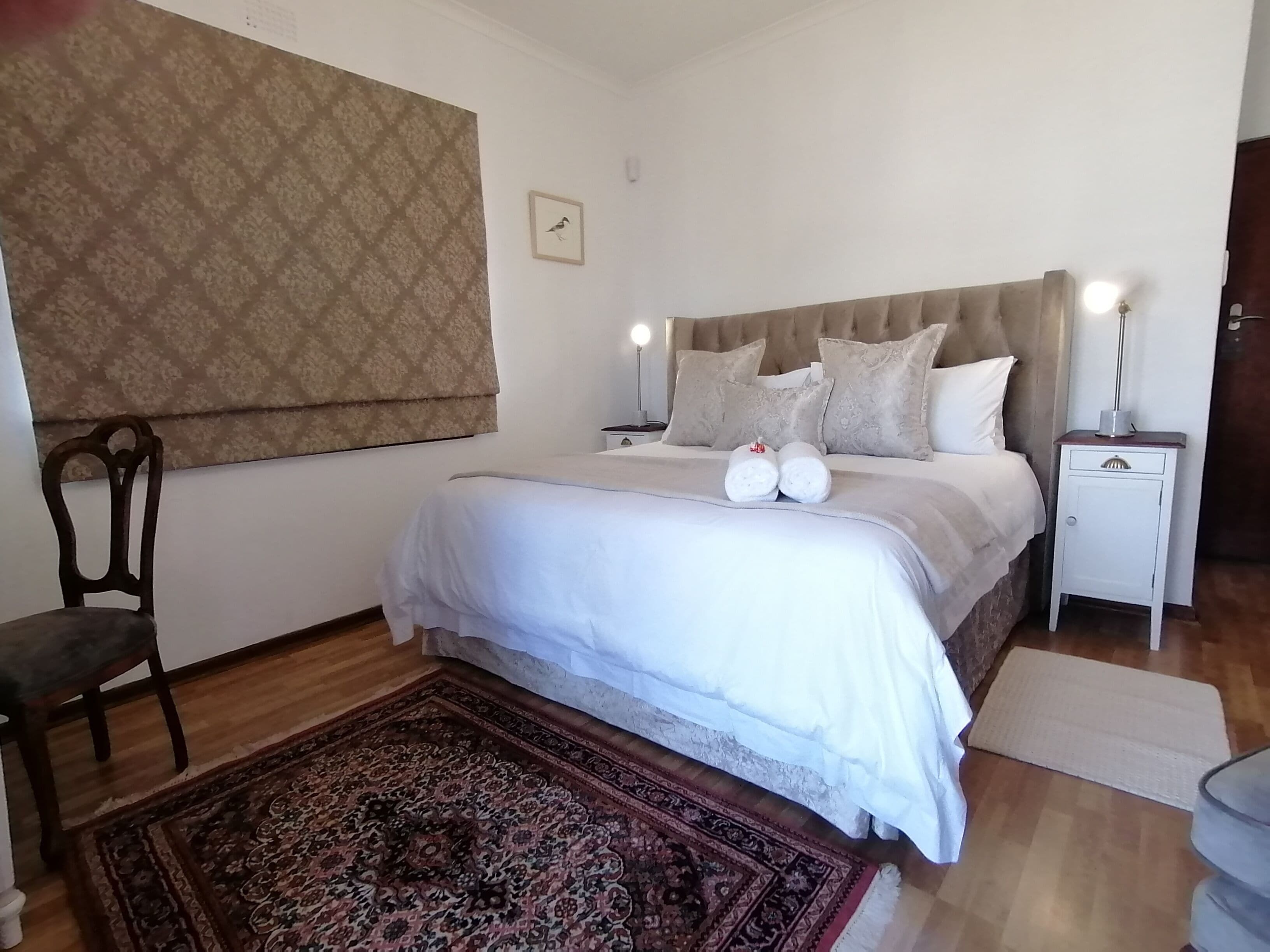 A neatly arranged bedroom with a large bed, two bedside tables, a chair, and a patterned rug.