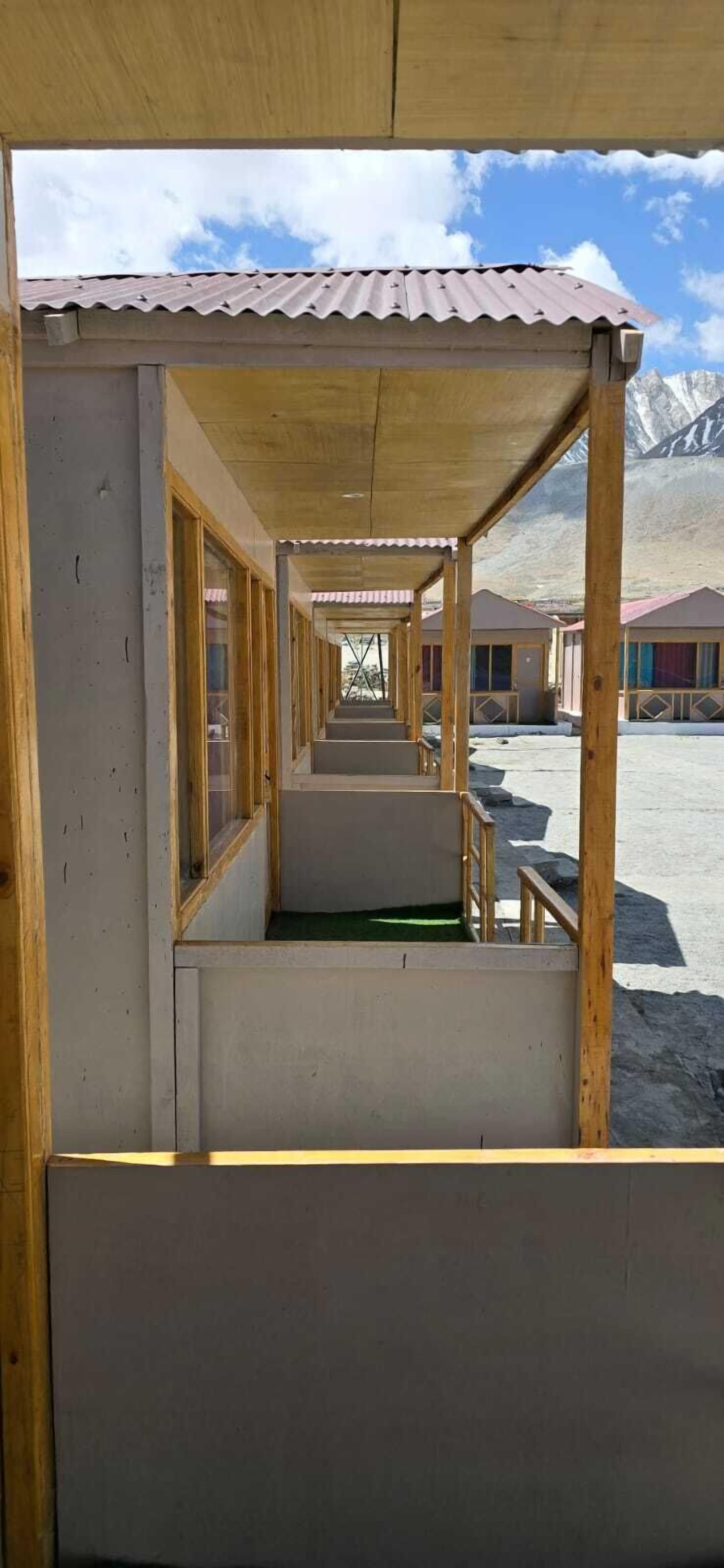 A corridor with wooden railings and a tiled roof, leading to multiple rooms with colorful facades.