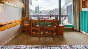 Un comedor con mesa y sillas, una ventana que ofrece vistas a edificios y montañas, y un radiador en la pared.
