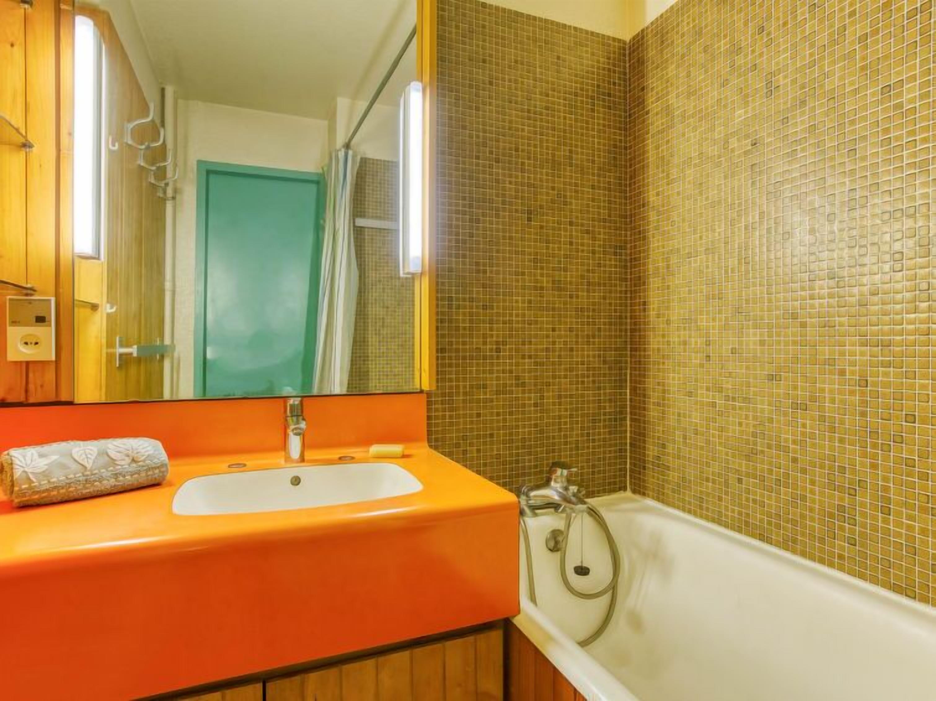 A bathroom with a wooden vanity, a white sink, a mirror, and a bathtub.
