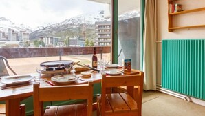 Un comedor con una mesa dispuesta para dos personas, vista a una montaña nevada y un radiador verde.