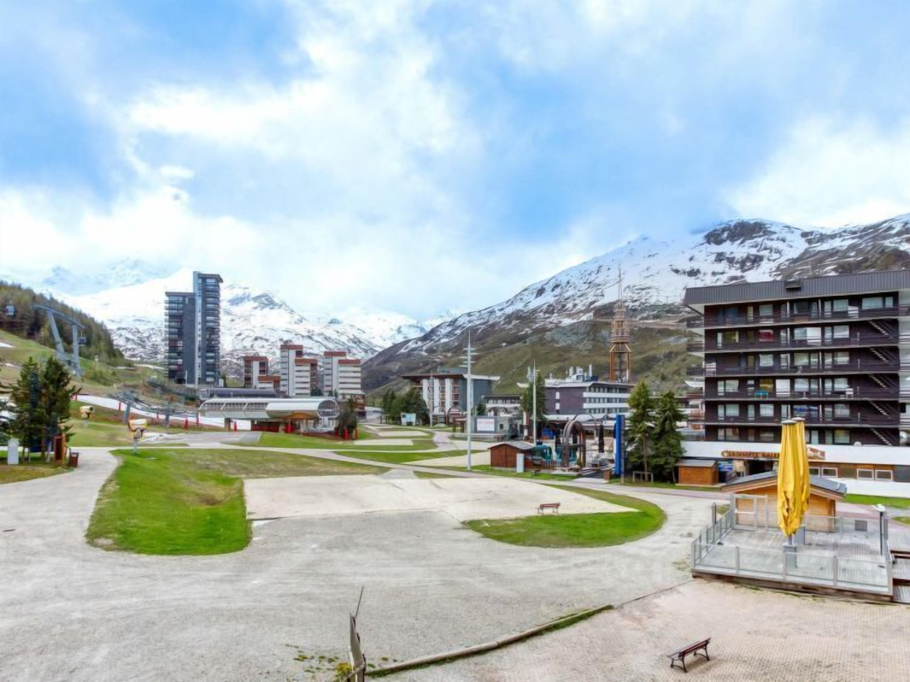 Un moderno complejo de edificios con varios pisos, rodeado de un amplio espacio exterior con senderos y vegetación, con montañas nevadas al fondo.