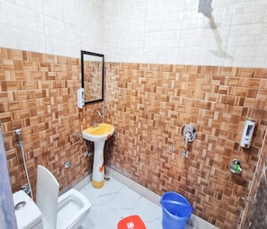 Une salle de bain avec un lavabo blanc, des toilettes et un seau bleu.