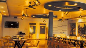 Restaurante com interior moderno, apresentando um bar com banquetas e um teto alto com luminárias circulares.