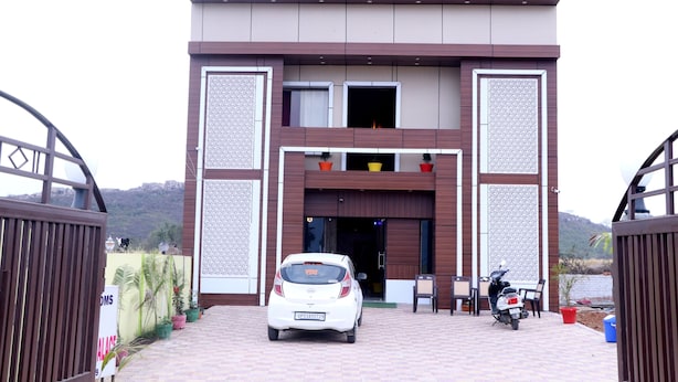 Entrada do Hotel Krishna Manu Palace, com um carro branco estacionado à frente e uma motocicleta à direita.