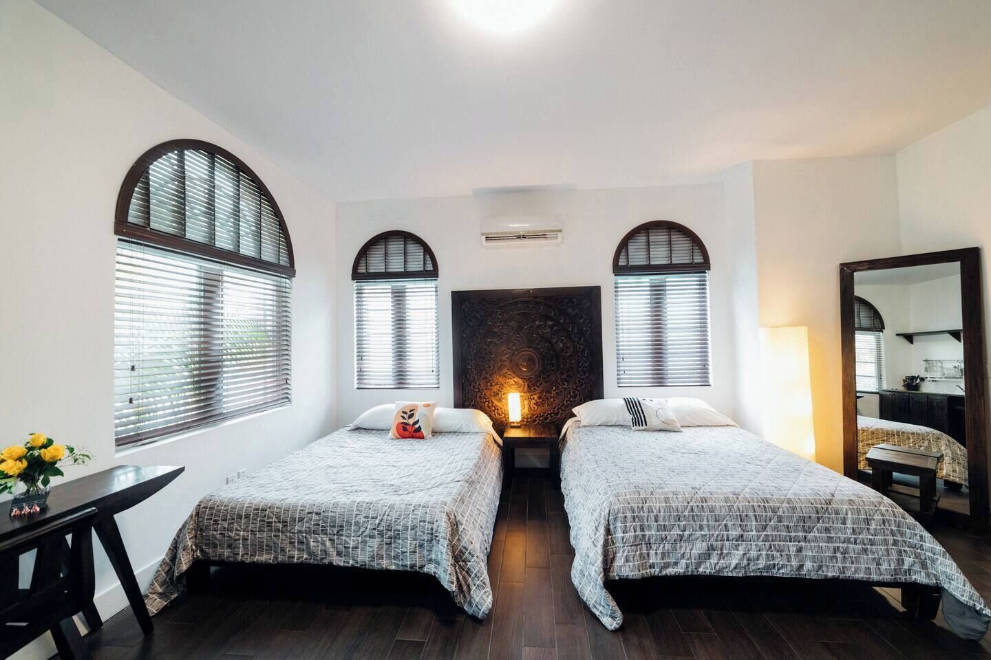 A room with two beds, a wooden floor, a large mirror, and a decorative wall panel.
