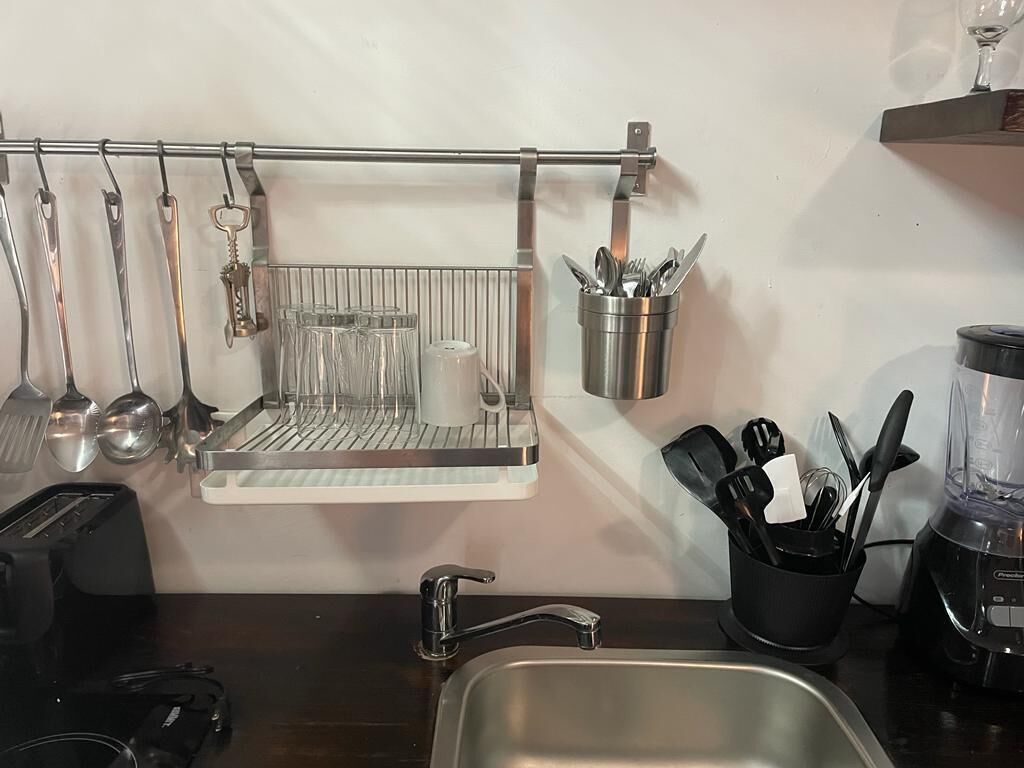 Une cuisine équipée d’un porte-ustensiles suspendu, d’un égouttoir à vaisselle, d’un mixeur et d’un évier.
