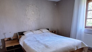 Un dormitorio con una cama de madera, una mesita de noche, decoración en la pared y una ventana con cortinas.