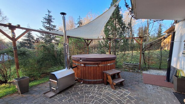 Un jacuzzi con revestimiento de madera, una banca de madera y una estructura de pérgola en un jardín.