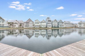 A waterfront property with a reflective pool, wooden deck, and a row of houses with distinct architectural styles. - Stunning Cinnamon Shore South Lakeside & Poolside Home With Amenities Galore (Port Aransas)