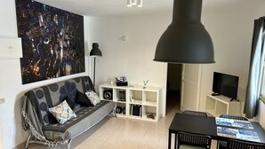 Ein Wohnzimmer mit einer Couch, einem Esstisch mit Stühlen, einem Fernseher und einem großen Gemälde an der Wand.