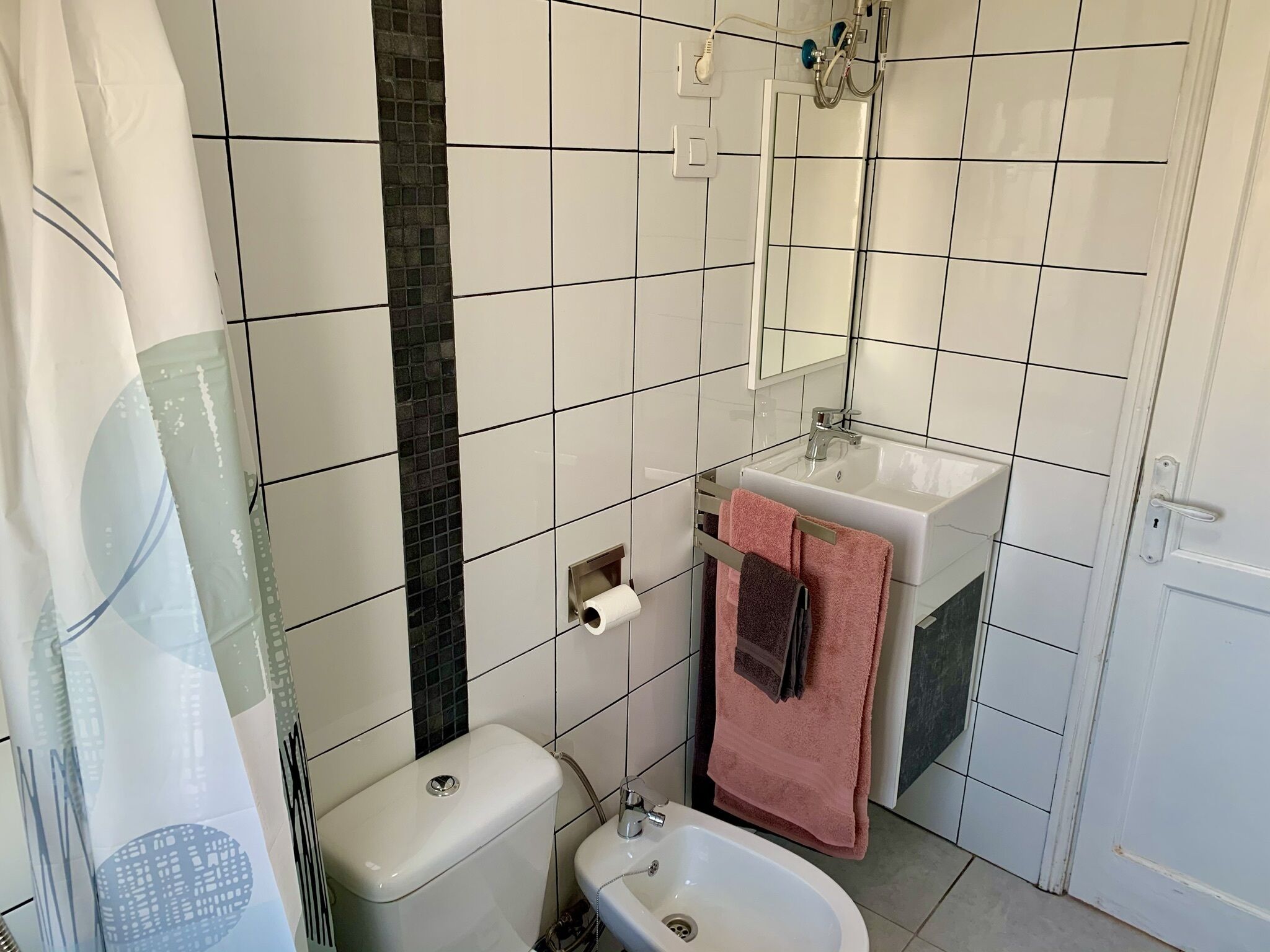 Een badkamer met witte tegels, een toilet, een wastafel met spiegel en een douchehoek.