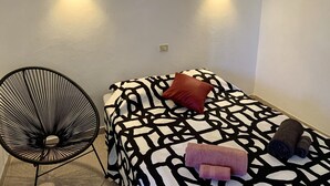 Ein kleiner, ordentlicher Raum mit einem Einzelbett, einem Sessel und zwei Wandleuchten.