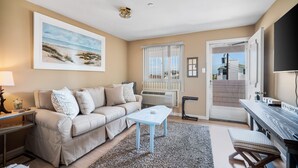 A living room with a beige sofa, a coffee table, a TV, and a large window with a view of the outside.