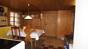 Ein Holzblockhaus-Interieur mit Esstisch, Stühlen, einer Küchenzeile und einem karierten Boden.
