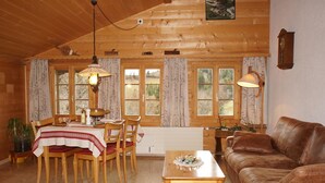 Ein gemütliches Blockhaus-Interieur mit Essbereich, Holzmöbeln und großen Fenstern, die einen Blick ins Freie bieten.