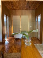 Un baño moderno con techo de madera, una bañera independiente y un florero de vidrio con una planta sobre una mesa de madera.