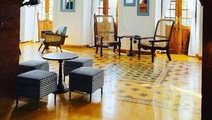 A spacious room with a high ceiling, arched windows, and a patterned floor. There are several chairs and a small table in the center. - The Postcard Saligao (Consua)