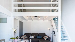 Un espace de vie moderne comprenant un coin repas, un ensemble de canapés aux couleurs sombres et un escalier avec des marches bleues.