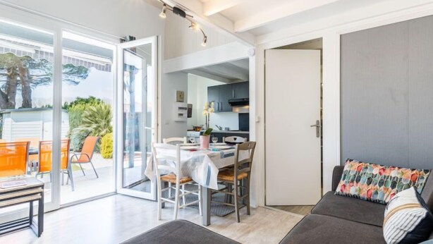 Un salon moderne avec un canapé, une table à manger et des chaises. On aperçoit un coin cuisine à travers une porte ouverte.