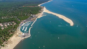 Vue aérienne d’une zone côtière comprenant un port de plaisance, une plage de sable et une végétation luxuriante environnante.