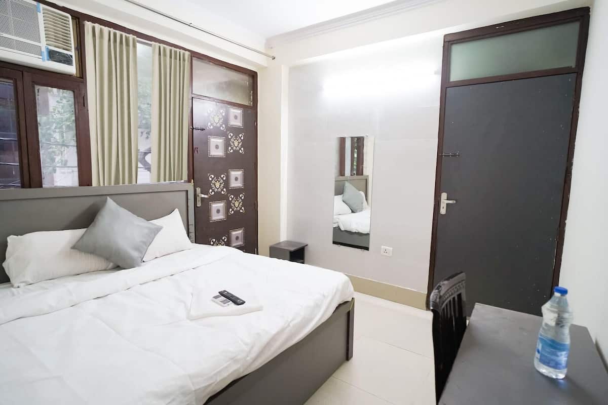 A hotel room with a bed, bedside table, water bottle, and a mirror on the wall.