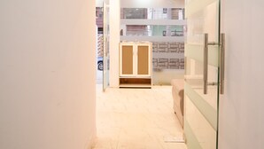 A modern hallway with a glass partition, a wooden cabinet, and a tiled floor. - Roomshala 034 Grihum Noida Sector 63 (Noida)