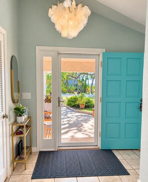 A foyer with a teal door, a white-framed mirror, a gold console table with a plant, and a black rug. - Paradise by the River - Relax in Style Near the Beach! Pool and Heated Spa (St. Augustine)