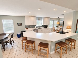 A modern kitchen with a large island, white cabinetry, and a dining area with wooden chairs. - Paradise by the River - Relax in Style Near the Beach! Pool and Heated Spa (St. Augustine)