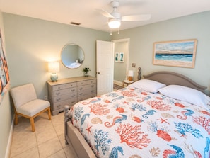 A bedroom with a bed, a chair, a dresser, a ceiling fan, and a painting on the wall. - Paradise by the River - Relax in Style Near the Beach! Pool and Heated Spa (St. Augustine)