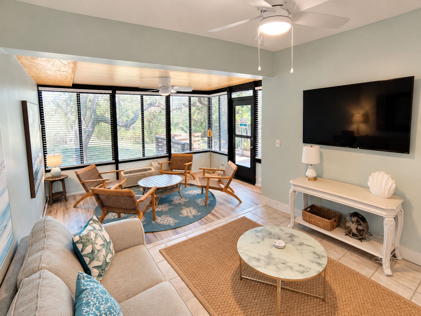 A living room with a sofa, coffee table, and chairs, a flat-screen TV, and a ceiling fan.