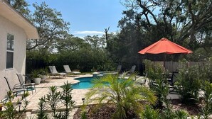 Ein Garten mit Swimmingpool, Liegestühlen und einem roten Sonnenschirm.