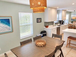 A modern kitchen with white cabinets, a dining area with a wooden table and chairs, and a large window with blinds. - Paradise by the River - Relax in Style Near the Beach! Pool and Heated Spa (St. Augustine)