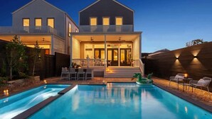Una casa de dos pisos con piscina, mobiliario exterior y terraza cubierta.