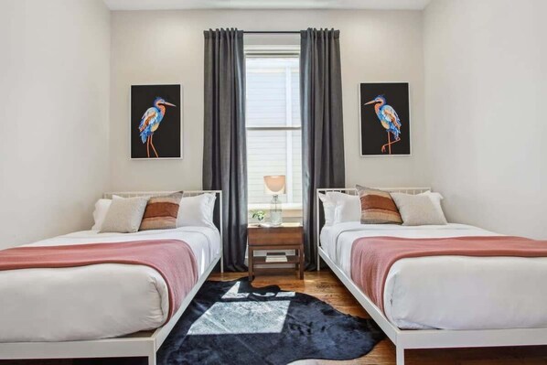 Une chambre double avec deux lits, une fenêtre avec des rideaux et deux tableaux représentant des oiseaux, accrochés au mur.