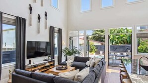 Una sala de estar moderna con un televisor de pantalla plana grande, sofás oscuros, una mesa de centro y una zona de bar con taburetes.