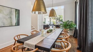 Un comedor con una larga mesa de madera, sillas de mimbre e iluminación colgante.