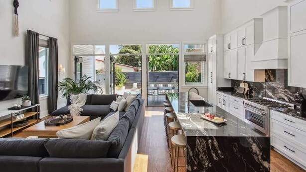Una cocina moderna con armarios blancos, una isla de mármol negro y un amplio ventanal con vistas a un jardín.