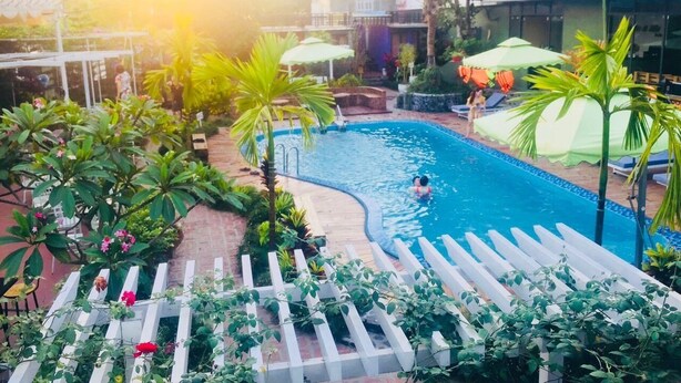 A swimming pool with a curved edge, surrounded by white pergolas and palm trees. - Mango Tree Homestay Cat Ba (Hai Phong)