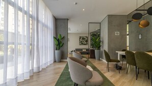 A modern living room with a sofa, dining area with chairs, large windows with sheer curtains, and potted plants. - SA1342 - Apartment 2 Suites Vila Nova Conceição (São Paulo)