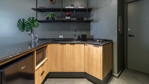 Eine moderne Küche mit einer Holzinsel, schwarzer Arbeitsplatte und integrierten Geräten. Über der Insel befinden sich Regale mit Dekoration und einem Blumentopf.