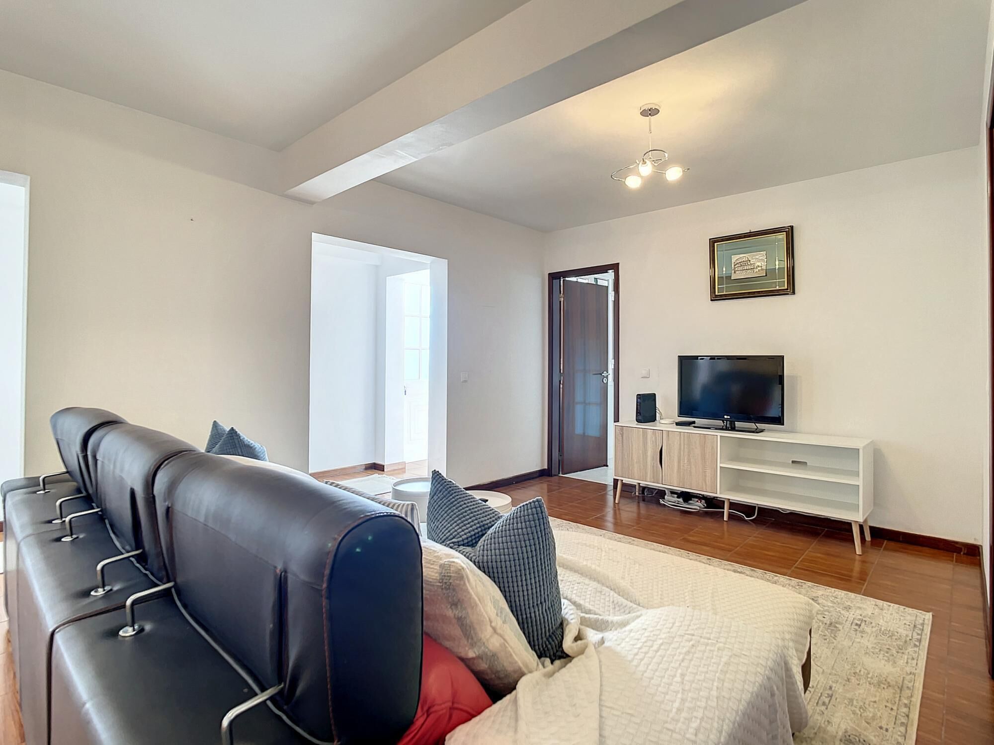 Una sala de estar moderna con un sofá de cuero negro, un mueble blanco para el equipo de entretenimiento con un televisor de pantalla plana y un cuadro en la pared.