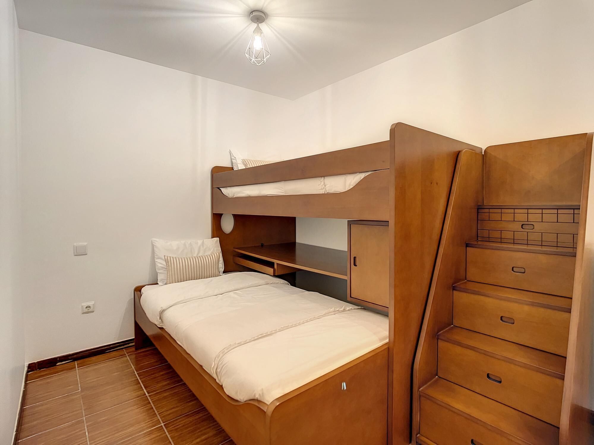 A compact room with a bunk bed, a small desk, and a wardrobe with multiple drawers.